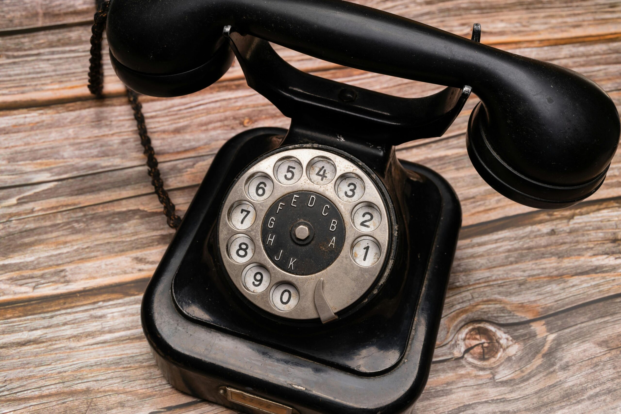Close-up of a classic black rotary dial telephone on a wooden background.